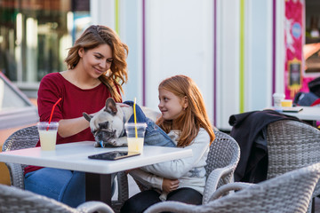 Mother and daughter enjoying with their French bulldog in cafeteria. 