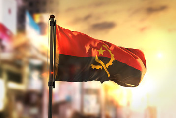 Angola Flag Against City Blurred Background At Sunrise Backlight - obrazy, fototapety, plakaty