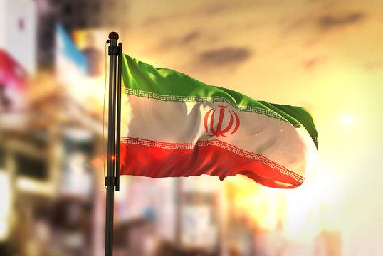 Iran Flag Against City Blurred Background At Sunrise Backlight