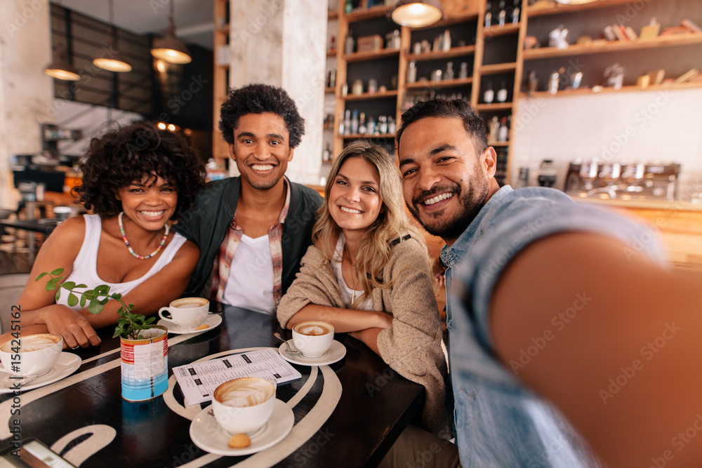 Poster Happy young man taking selfie with friends in a cafe