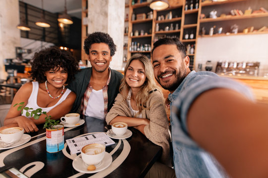 Happy young man taking selfie with friends in a cafe
