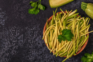 Raw zucchini pasta on dark background.