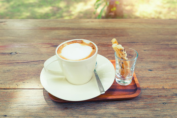 Coffee cup and pastry on wooden table with nature background.