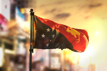 Papua New Guinea Flag Against City Blurred Background At Sunrise Backlight