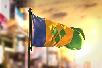 Saint Vincent and the Grenadines Flag Against City Blurred Background At Sunrise Backlight