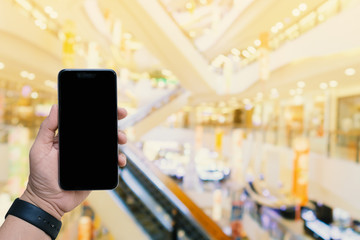 hand holding blank screen smartphone with blurred shopping mall background for concept internet of things; smart life; digital online.