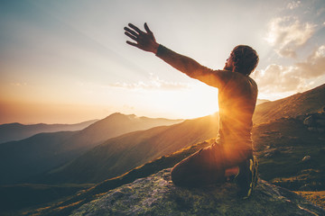 Man praying at sunset mountains raised hands Travel Lifestyle spiritual relaxation emotional concept vacations outdoor harmony with nature landscape