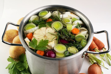 Broth with carrots, onions various fresh vegetables in a pot - colorful fresh clear spring soup. Rural kitchen scenery vegetarian bouillon or stock