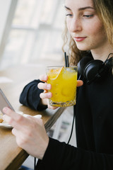 Young trendy woman holding an orange cocktail and listening to music