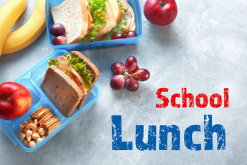 Lunchboxes with sandwiches and different products on grey background