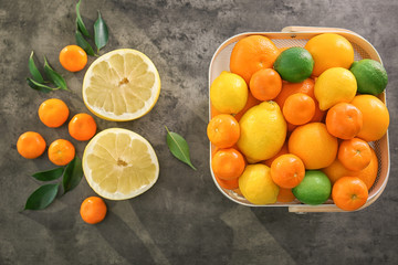 Plastic basket with fresh citrus fruits and halves of pomelo on table