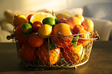 Metal basket full of different citrus fruits on table