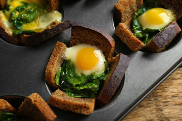 Baking mold with eggs and spinach on wooden table