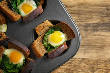 Baking mold with eggs and spinach on wooden table