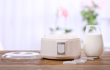 Modern yogurt maker and glass jug with milk on wooden table