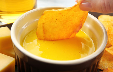 Woman dipping chips into bowl with creamy cheese sauce, close up