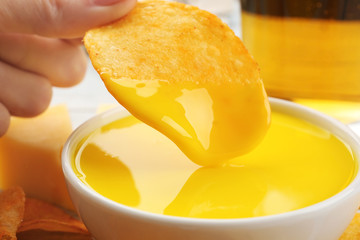 Dipping chips into bowl with creamy cheese sauce, close up