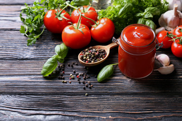 Composition of ketchup in jar and ingredients on wooden background