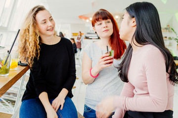 Three young girlfriends chatting while drinking coktail on free time