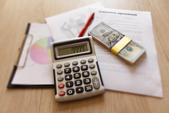 Insurance form with pen, dollars, calculator on the table. Homeowner insurance policy