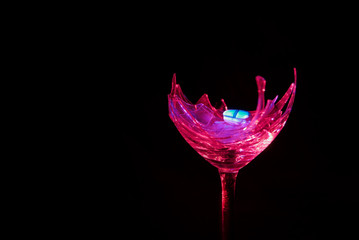 Alcoholism and drag abuse, blue pill on pink broken wine glass on black background - obrazy, fototapety, plakaty