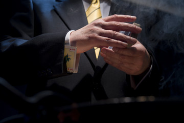 The man in a suit shuffles cards, in his sleeve he has a diamond ace, cigarette smoke. - obrazy, fototapety, plakaty