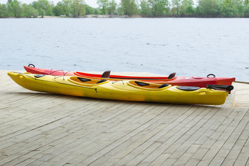 Two kayak boats on wooden deck at station near water