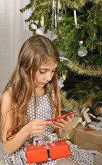Mädchen liest Weihnachtskarte unterm Weihnachtsbaum