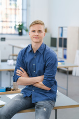selbstbewusster junger mann sitzt im büro auf dem schreibtisch
