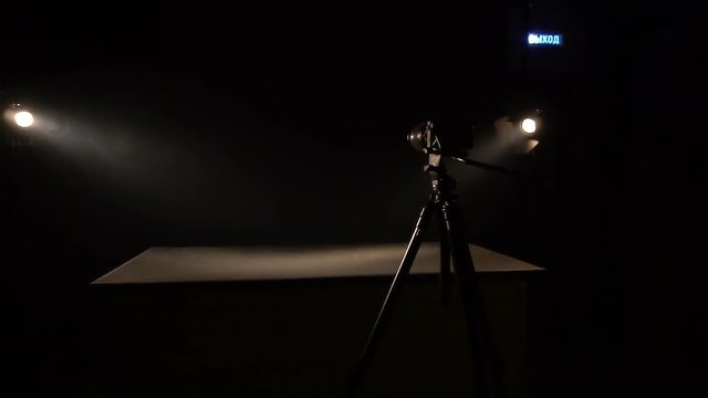 Table in a darkened room, with a photocamera nearby. Black background. Strained and awesome frame. Room for interrogation.