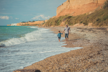 Dad and son walking along the seashore. Dad and son walking along the shore of the ocean. Weekend at the beach. A beach Stone. A sea foam.