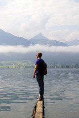 Travel to Sankt-Wolfgang, Austria. The young man are walking on a bridge with the view on the lake near to mountains in the cloudy weather.