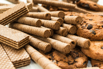 Chocolate waffle rolls, biscuits and classic waffle on a wooden white table. Sweet-toothers.