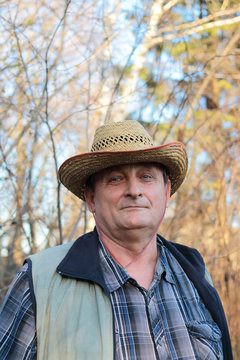 A handsome elderly man in a cowboy hat and plaid shirt is a real cowboy, with a pretty enough look at the camera. Satisfied pensioner