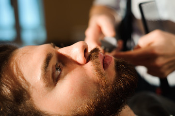 Naklejka premium Master cuts hair and beard of men in the barbershop