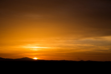 Beautiful sunset with half of the sun coming down behind some mountains and orange tones in the sky and clouds