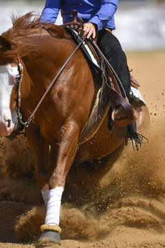 The close-up view of a rider in cowboy chaps and boots sliding the horse in the sand