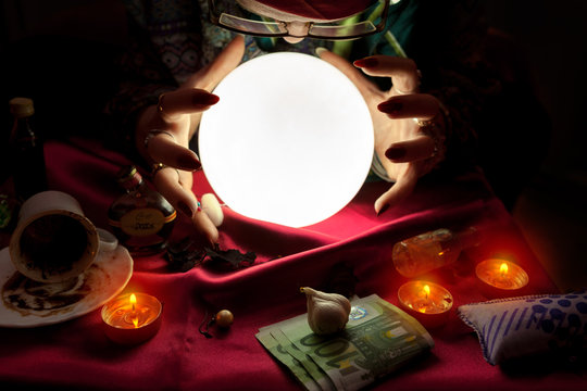 Fortune teller woman looking at crystal ball with her hands around crystal ball