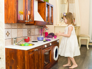 Active little preschool age child, cute toddler girl with blonde curly hair, shows playing kitchen, made of wood, plays in the kitchen