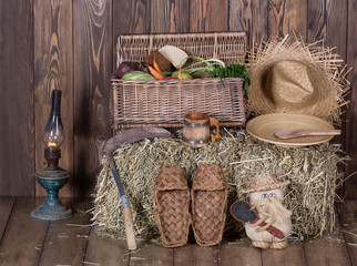 Basket with vegetables, bast shoes, hay, straw hat in an old barn