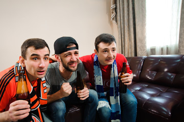 Young men drink beer, eat chips and root for football