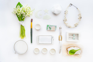 Beauty blog concept. Female styled accessories: smartfone, watches, necklace, cosmetic and bouquet of may-lily flowers on white background. Flat lay, top view trendy fashion background. Space for text