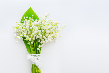 Beautiful bouquet of lilies of the valley, may-lily flowers with lace ribbon on the white background, top view. Selective focus. Space for text.