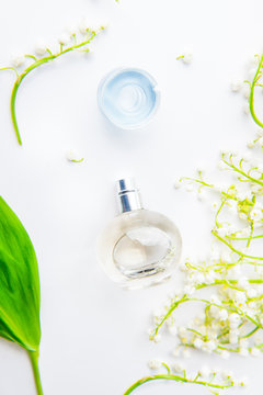 Beauty concept. Flat lay with Orbicular perfume bottle surrounded by fresh lilies of the valley, may-lily flowers and green leaf on the white background. Top view. Selective focus
