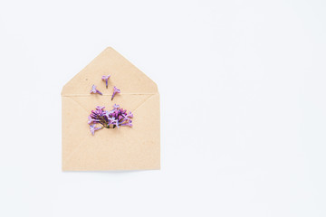 White Card with opened craft paper envelope filled with spring blossom purple lilac flowers laying on white background. top view. Concept of love and proposal. Flat lay. Space for text.