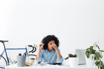 Stressed and frustrated young dark-skinned businesswoman feeling tired and sleepy while doing...