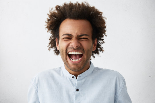 Feeling so angry! Studio shot of stressed and furious African American businessman in shirt shouting loudly in despair and anger feeling fed-up with his employees or facing problems at work