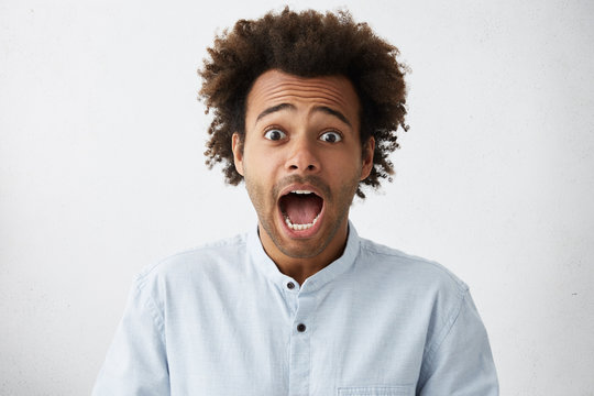 Afraid young Afro American male employee raising eyebrows and screaming with mouth wide opened, having shocked scared look after he forgot important papers at home. Human emotions and feelings