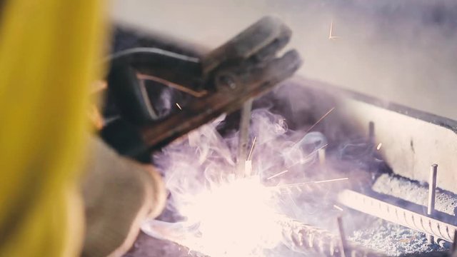 Close-up slow motion shot of a worker welding as sparks fly. Welderor industrial grinder at work in factory plant. Welders repairing heavy equipment for the construction industry.