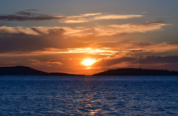 Sunset on the blue sea with clouds. The sun between clouds. 